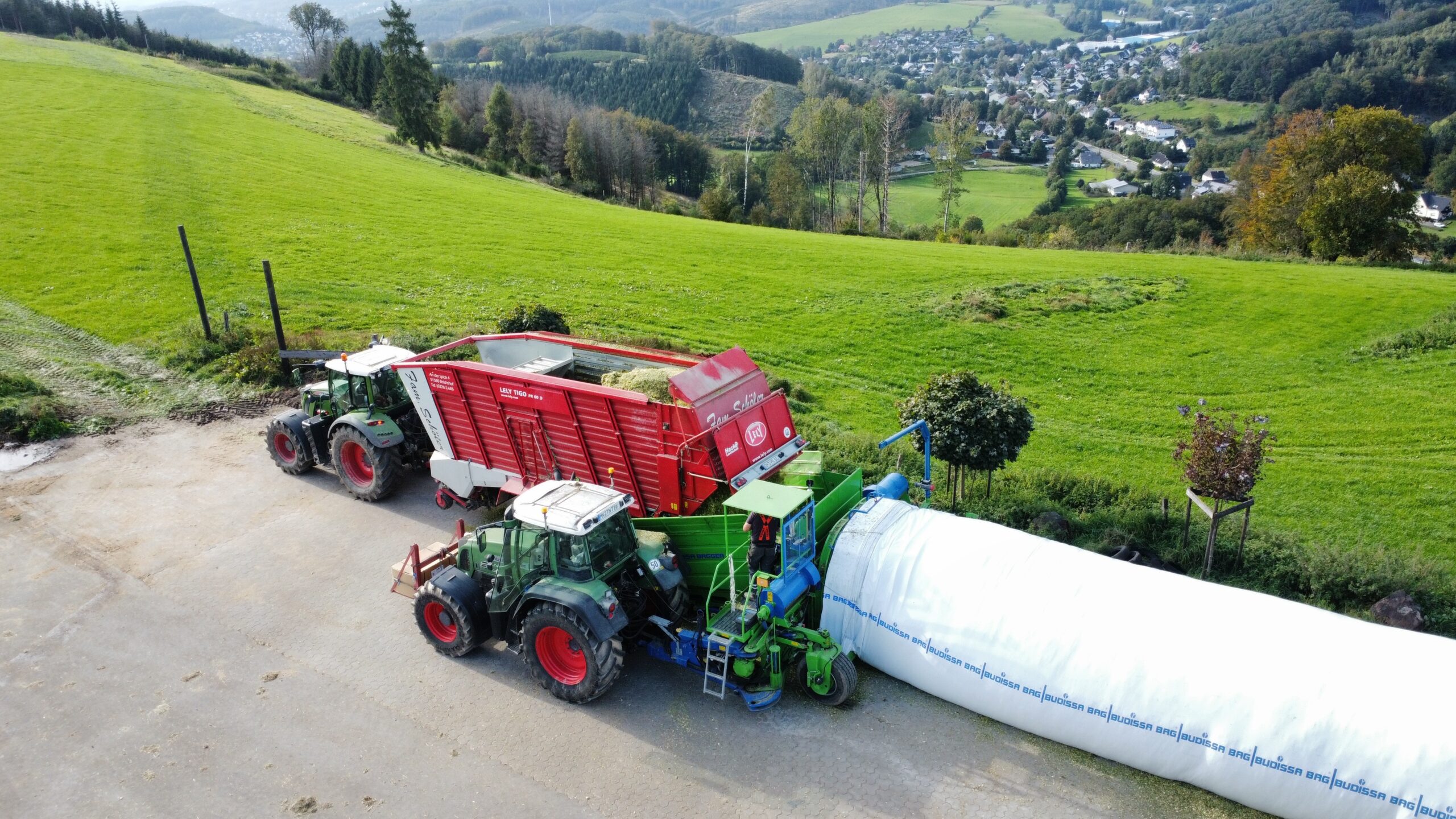 Dronenbild von zwei Treckern, einem Ladewagen und der Siloschlaucpresse